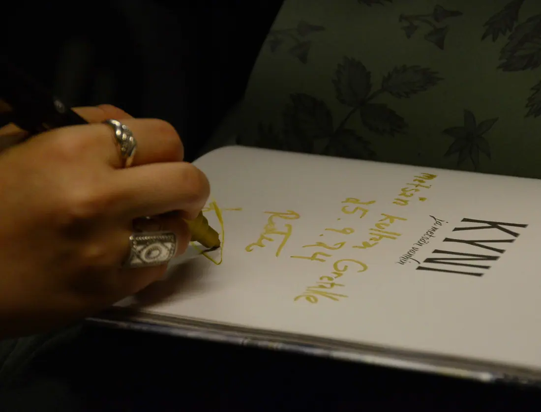 Käsi signeeraa Kyni ja metsän vanhin -kirjaa kultaisella musteella.